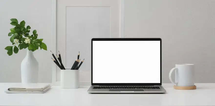 Escritorio de trabajo ordenado con un portátil abierto, cuaderno, lápices y una planta, que representa el entorno profesional de un asesor de seguros en Tenerife